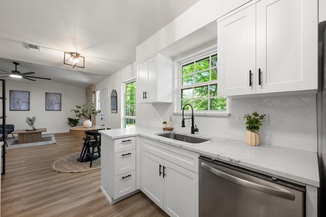 kitchen featuring stainless steel dishwasher, a sink, tasteful backsplash, white cabinets, and vaulted ceiling