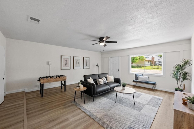 living room featuring light wood-style flooring, ceiling fan, a textured ceiling, and baseboards