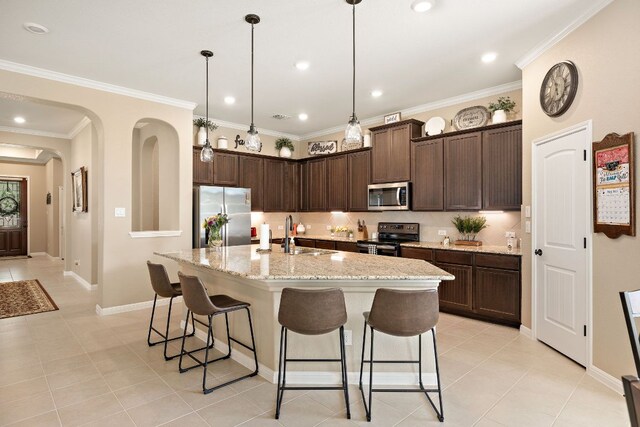 417 Freeman Park Pl, Round Rock, TX 78665 - kitchen with appliances with stainless steel finishes, a breakfast bar area, dark brown cabinets, light tile patterned floors, and crown molding