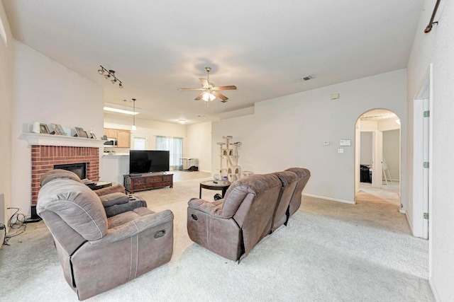 living area featuring arched walkways, a ceiling fan, light colored carpet, and a fireplace