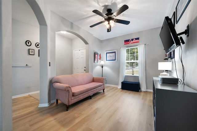sitting room with arched walkways, light wood-style flooring, a ceiling fan, and baseboards