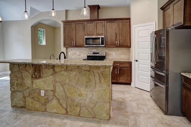 kitchen with stainless steel appliances, backsplash, arched walkways, light stone countertops, and decorative light fixtures