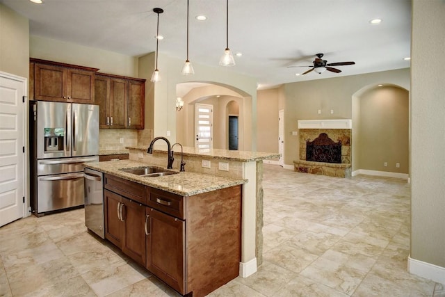 kitchen with stainless steel appliances, a sink, arched walkways, ceiling fan, and light stone countertops