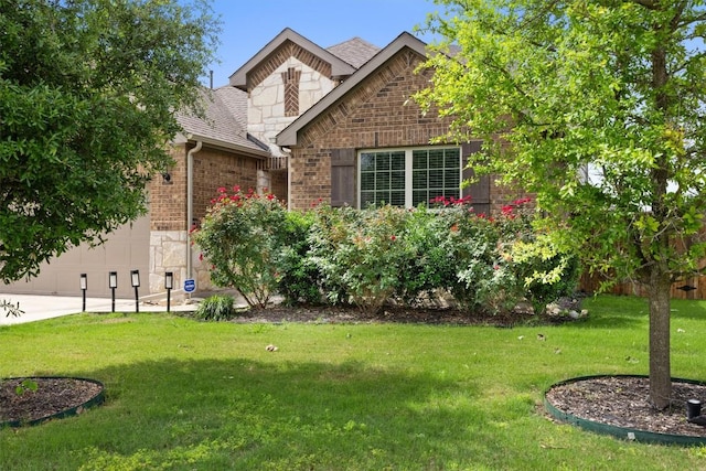 view of front of property featuring brick siding, a shingled roof, a front lawn, a garage, and stone siding