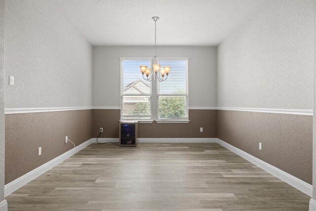 unfurnished dining area featuring a chandelier, a textured wall, light wood-style flooring, and baseboards