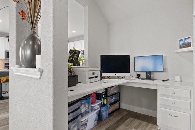 office area featuring wood finished floors, vaulted ceiling, built in desk, and baseboards