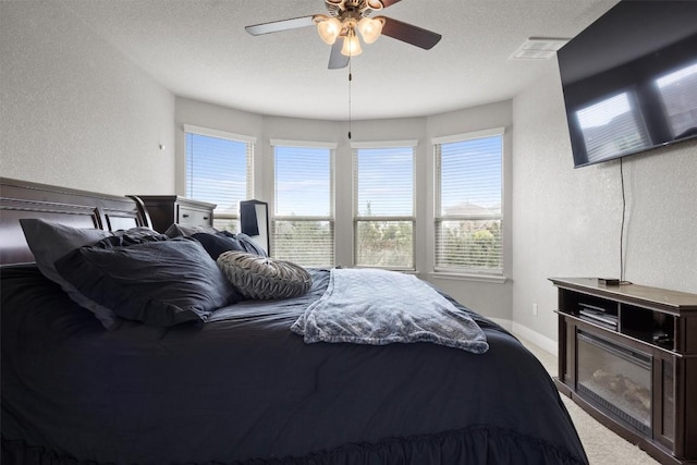 bedroom featuring a textured wall, light carpet, a ceiling fan, and a textured ceiling