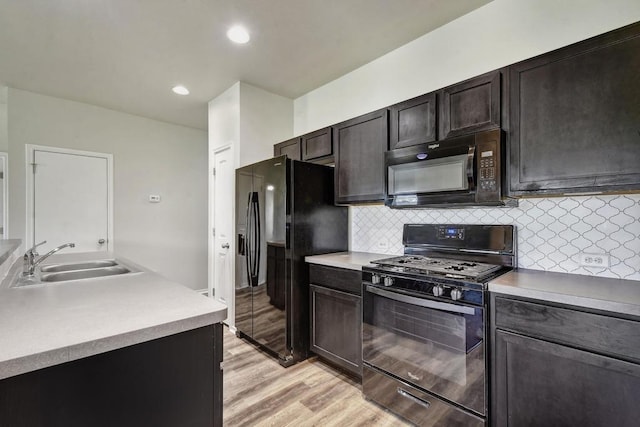 kitchen with black appliances, a sink, light wood-style flooring, decorative backsplash, and recessed lighting