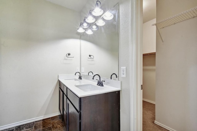 bathroom with baseboards, double vanity, and a walk in closet