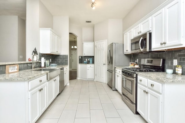 kitchen with appliances with stainless steel finishes, decorative backsplash, a sink, white cabinetry, and arched walkways