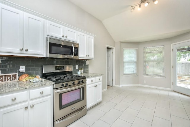 kitchen with appliances with stainless steel finishes, backsplash, baseboards, vaulted ceiling, and white cabinetry