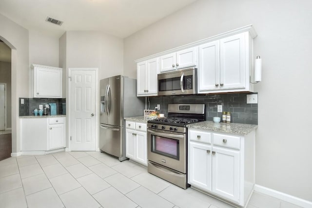 kitchen featuring stainless steel appliances, arched walkways, decorative backsplash, white cabinets, and light stone countertops