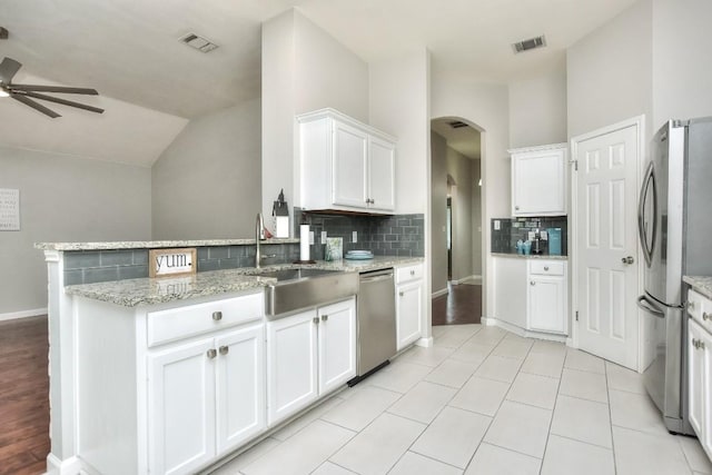 kitchen featuring stainless steel appliances, a sink, a ceiling fan, decorative backsplash, and arched walkways