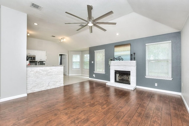 unfurnished living room featuring lofted ceiling, a ceiling fan, wood finished floors, baseboards, and a brick fireplace
