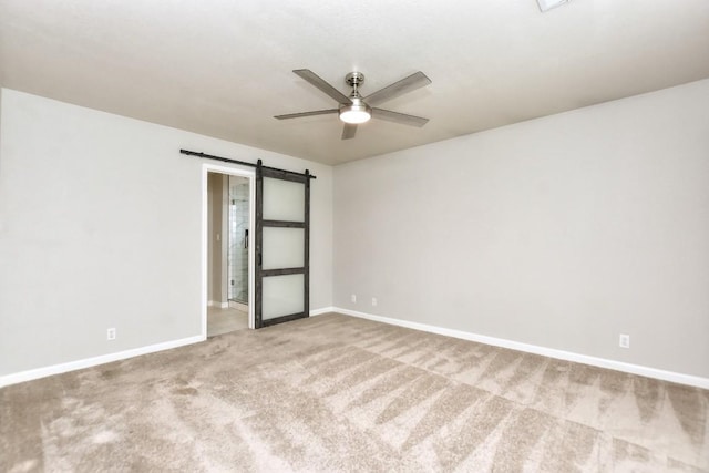 empty room featuring a barn door, a ceiling fan, carpet, and baseboards