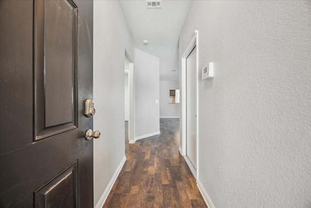 corridor with dark wood finished floors, baseboards, and a textured wall