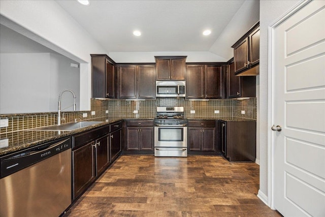 kitchen featuring stainless steel appliances, a sink, dark stone counters, dark brown cabinets, and recessed lighting