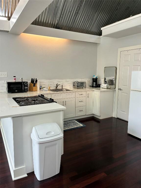 101 Short St, Smithville, TX 78957 - kitchen with freestanding refrigerator, cooktop, dark wood-style floors, white cabinets, and a peninsula