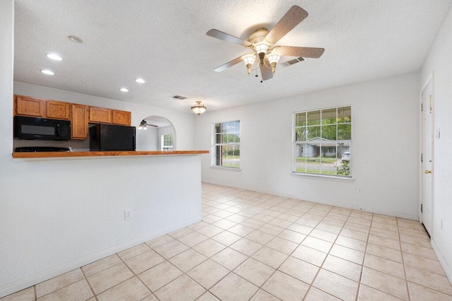 8309 Burrell Dr, Austin, TX 78757 - kitchen with black microwave, fridge, a ceiling fan, a textured ceiling, and brown cabinets