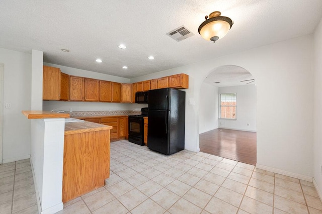 8309 Burrell Dr, Austin, TX 78757 - kitchen with black appliances, arched walkways, a peninsula, light tile patterned flooring, and recessed lighting