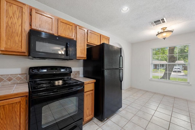 8309 Burrell Dr, Austin, TX 78757 - kitchen with black appliances, tile counters, a textured ceiling, light tile patterned flooring, and brown cabinets