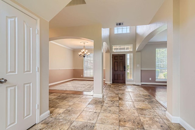 entrance foyer featuring baseboards, arched walkways, crown molding, a chandelier, and stone tile floors