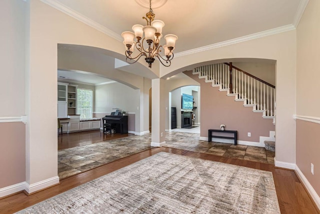 living area featuring arched walkways, wood finished floors, crown molding, a chandelier, and baseboards
