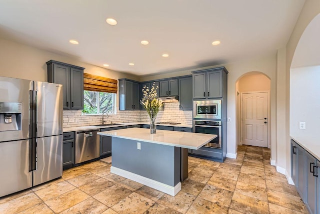 kitchen with stainless steel appliances, arched walkways, a sink, light countertops, and decorative backsplash
