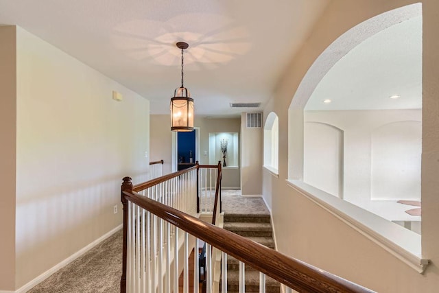 hall featuring carpet flooring, baseboards, and an upstairs landing