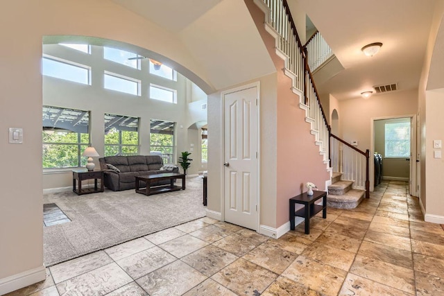 entrance foyer with a towering ceiling, baseboards, arched walkways, light carpet, and stairs