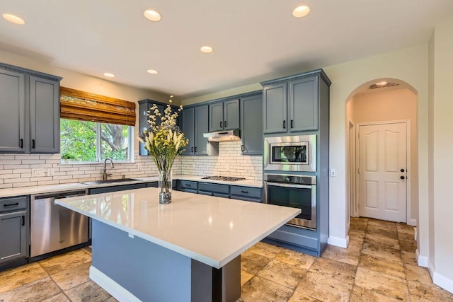 kitchen with appliances with stainless steel finishes, a sink, arched walkways, light countertops, and decorative backsplash