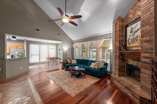 living room featuring high vaulted ceiling, a fireplace, a ceiling fan, a textured ceiling, and wood finished floors