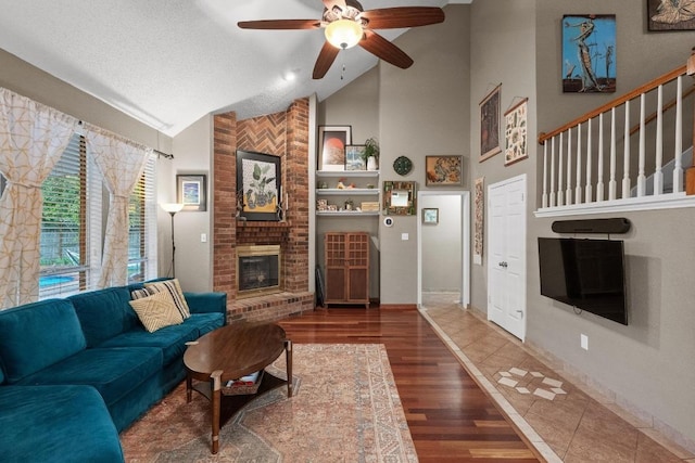 living room with lofted ceiling, a fireplace, wood finished floors, a ceiling fan, and a textured ceiling