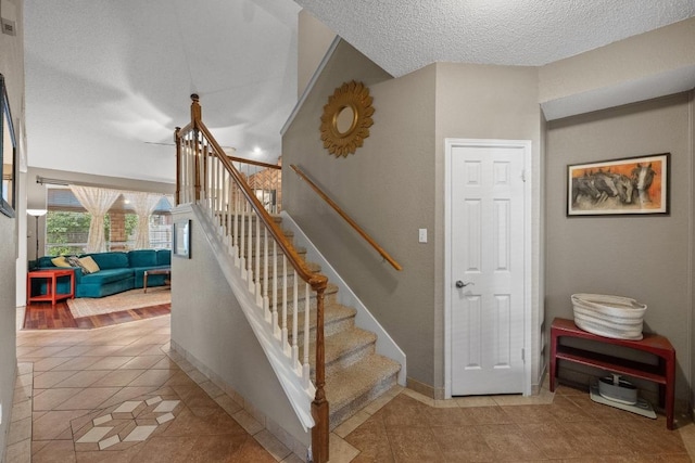 staircase with tile patterned floors, a textured ceiling, and baseboards