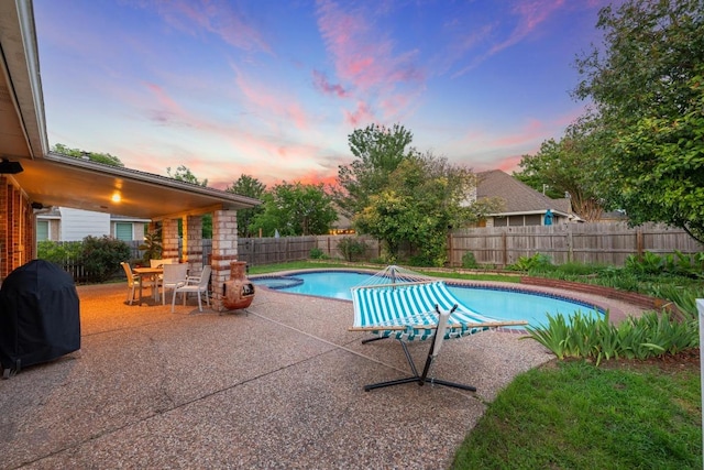 pool at dusk featuring grilling area, a patio area, and a fenced backyard