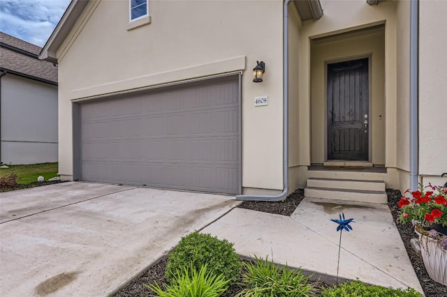 doorway to property featuring stucco siding, a garage, and concrete driveway