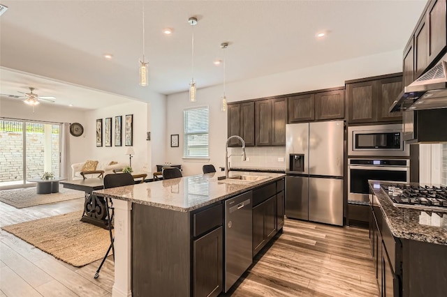 4608 Modena Bay Bnd, Leander, TX 78641 - kitchen with stainless steel appliances, light wood-type flooring, stone countertops, dark brown cabinetry, and a kitchen breakfast bar
