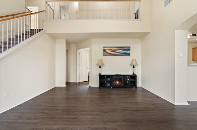 13306 James Monroe St, Manor, TX 78653 - unfurnished living room featuring dark wood finished floors, a towering ceiling, baseboards, arched walkways, and stairway