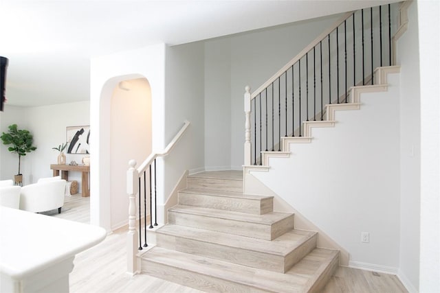 stairway featuring wood finished floors, baseboards, and arched walkways
