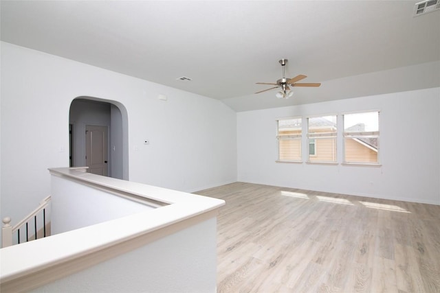 unfurnished room with ceiling fan, light wood-style flooring, arched walkways, vaulted ceiling, and baseboards