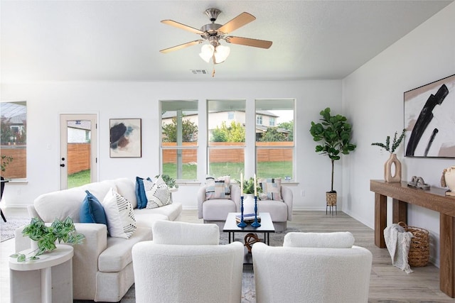 living room with light wood-type flooring, a ceiling fan, and baseboards