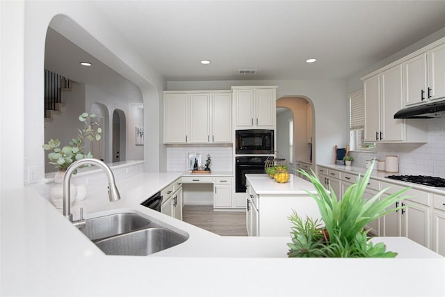 kitchen with black appliances, under cabinet range hood, a sink, decorative backsplash, and recessed lighting