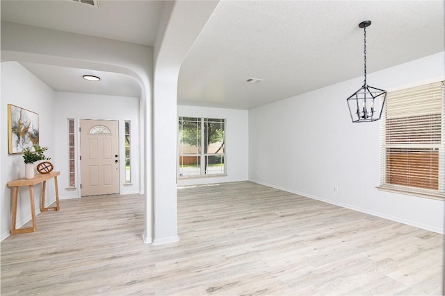 foyer entrance with light wood-style flooring, arched walkways, a chandelier, and baseboards