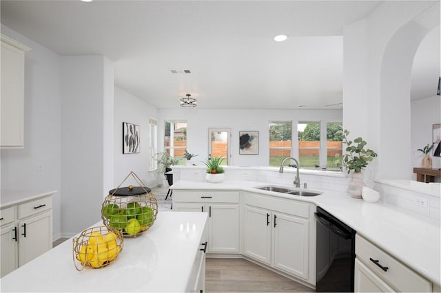 kitchen featuring a sink, dishwasher, arched walkways, light countertops, and a peninsula