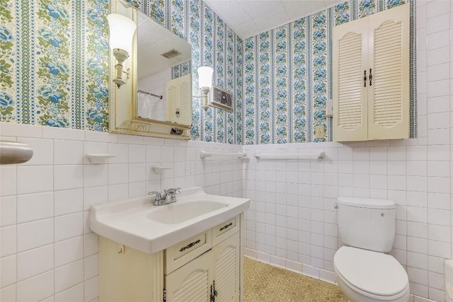 503 Colorado St, Smithville, TX 78957 - full bath featuring wallpapered walls, wainscoting, toilet, tile walls, and vanity