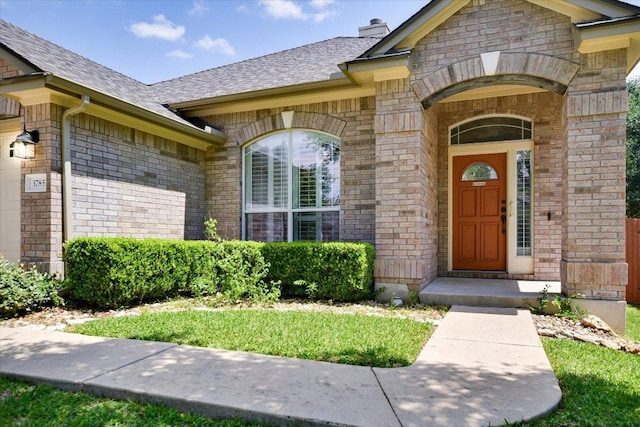 doorway to property with a chimney, a shingled roof, a garage, and brick siding