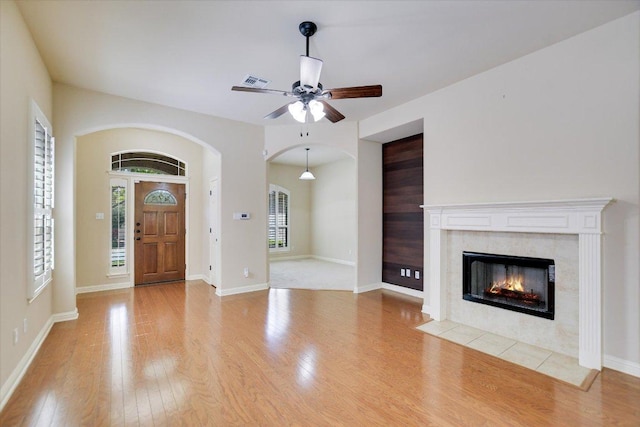 foyer entrance with arched walkways, wood finished floors, ceiling fan, a tile fireplace, and baseboards