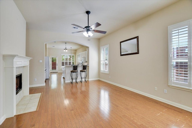 living room featuring a ceiling fan, arched walkways, light wood finished floors, baseboards, and a fireplace