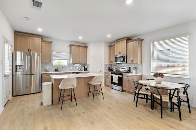 615 Backstays Loop, Kyle, TX 78640 - kitchen featuring stainless steel appliances, a center island, light wood finished floors, a kitchen bar, and decorative backsplash