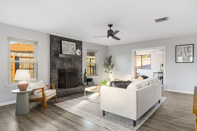 living room featuring wood finished floors, baseboards, a ceiling fan, and a stone fireplace